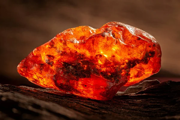 Beauty of natural raw amber. A piece of yellow-red transparent natural amber on piece of stoned wood — Stock Photo, Image