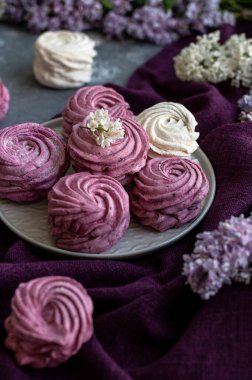Frenk üzümünden ve elmadan yapılmış ev yapımı marşmelovlar leylak dolgusu arasında bir tabakta duruyor. Fotoğraf siyah bir anahtarda..