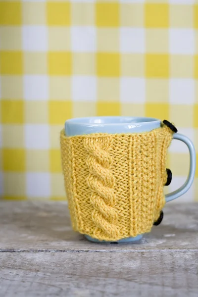 Blaue Tasse im gelben Pullover auf gelbem Hintergrund — Stockfoto