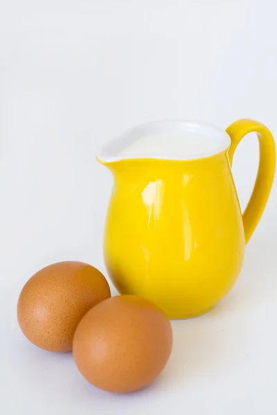 Caraffa gialla con latte e uova su fondo bianco — Foto Stock