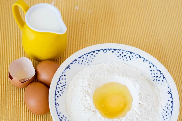 Piatto con farina, uova e brocca di latte in piedi su uno sfondo giallo — Foto Stock