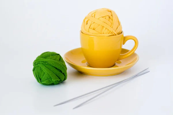 Gelbe Tasse, zwei Knäuel Garn und Stricknadeln hell liegend — Stockfoto