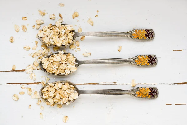 Tres cucharadas de avena sobre un fondo de madera blanca . —  Fotos de Stock