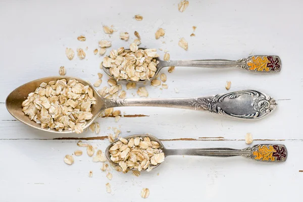 Tres cucharadas de avena sobre un fondo de madera blanca . —  Fotos de Stock