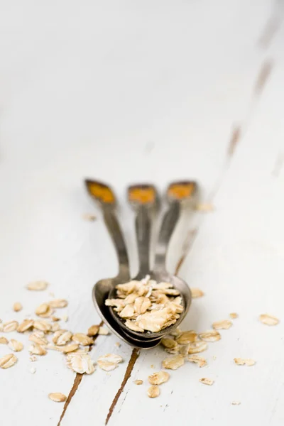 Three tablespoons of oatmeal lying on a white wooden background. — Stock Photo, Image