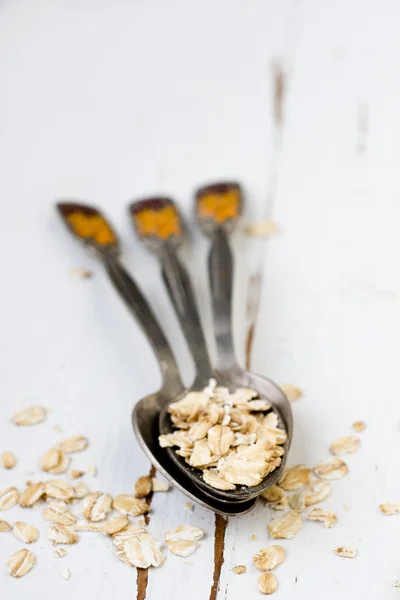 Three tablespoons of oatmeal lying on a white wooden background. — Stock Photo, Image