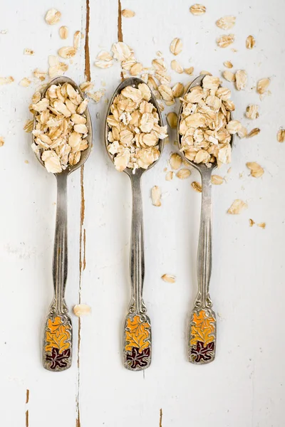 Three tablespoons of oatmeal lying on a white wooden background. — Stock Photo, Image