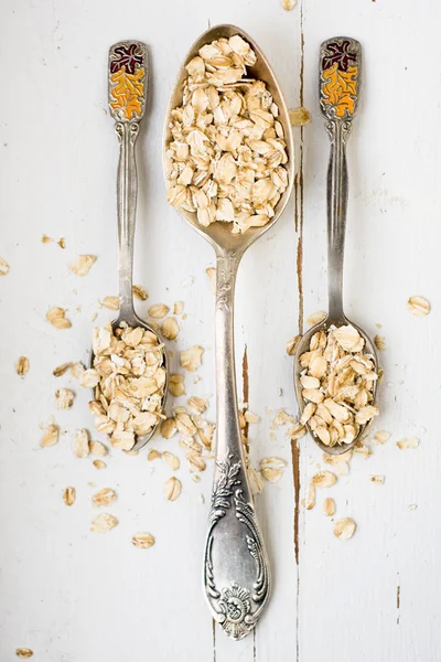 Three tablespoons of oatmeal lying on a white wooden background. — Stock Photo, Image