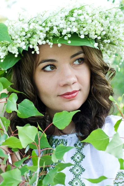 Portret van een jonge mooie in traditionele Oekraïens geborduurd shirt en een krans van lelies van de vallei op het hoofd — Stockfoto