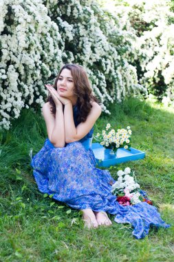 Çimen çiçekler arasında oturan mavi elbiseli kız