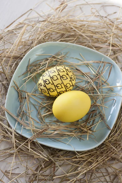 Œufs de Pâques dans une assiette de paille sur fond blanc — Photo