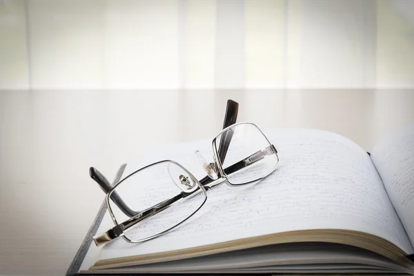 Brillen zet op een boek met op het Bureau — Stockfoto