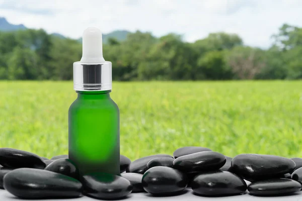 Serum oil bottle dropper mock up or essential oil with black stone agent green grass field