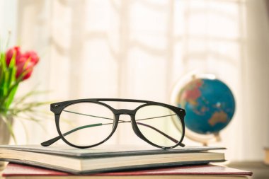Okuma gözlükleri pencerenin yanındaki ahşap masanın üzerine serili ciltli kitaplar.