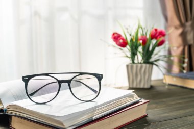 Okuma gözlüklerini pencerenin yanındaki tahta masanın üzerine koy.