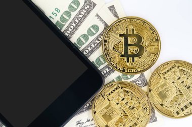 Üst Manzara Bitcoins madeni parası ve 100 dolarlık akıllı telefon banknotları. Metal parlayan bitcoin şifreleme paraları ve Amerikan dolarını kapat