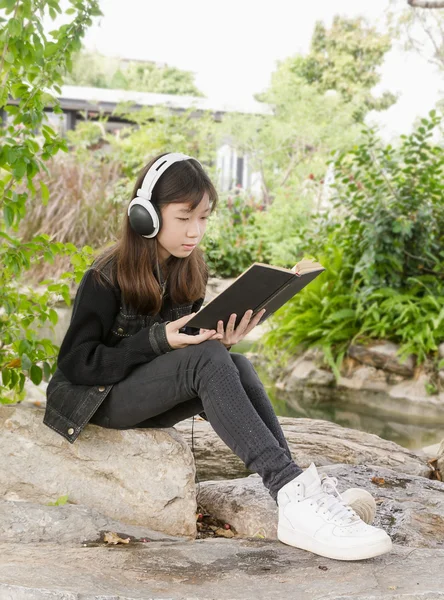 読んでいる若い女の子を予約して公園で音楽を聴く — ストック写真