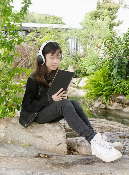 Młoda dziewczyna czytanie dokonać rezerwacji i słuchać muzyki w parku — Zdjęcie stockowe