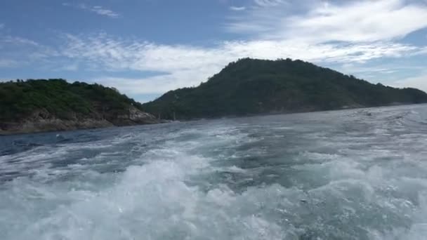 Waves splash behind boat and tropical island afar — Stock Video
