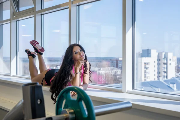 På gym. Athletic brunett poserar på fönsterbrädan — Stockfoto