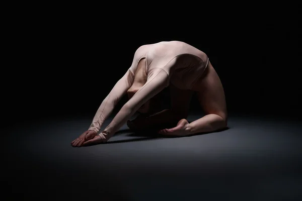 Flexible female gymnast exercising in dark studio — Stock Photo, Image