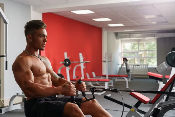 En el gimnasio. Sexy sin camisa chico ejercitando en simulador —  Fotos de Stock