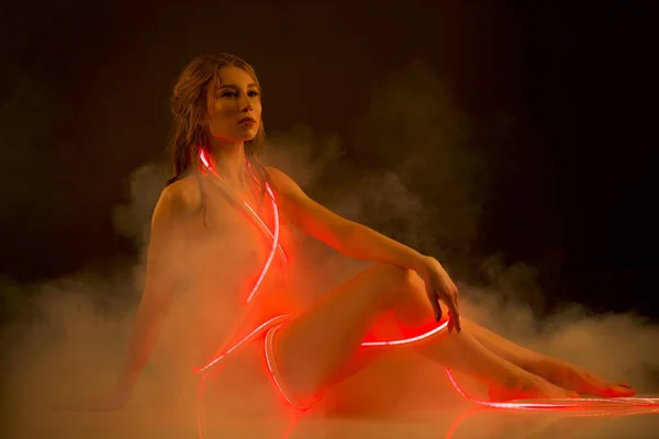 Изящная обнаженная женщина с красной неоновой светлой полосой в студии — стоковое фото