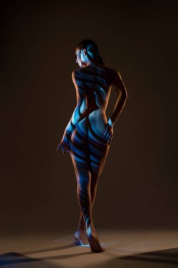 Çıplak kadın çizgili ışıkla karanlık stüdyoda yürür.