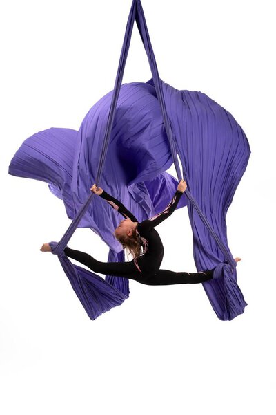 Flexible woman doing aerial silks trick on fabric