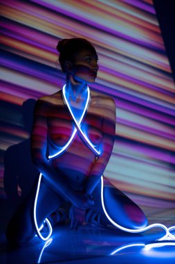 Aydınlatılmış stüdyoda neon kayışlı çıplak bir kadın.