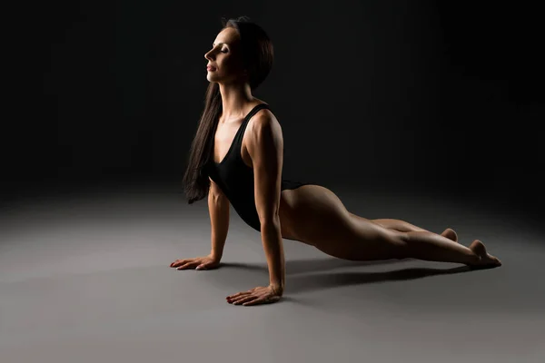 Graceful woman in bodysuit in dark studio — Stockfoto