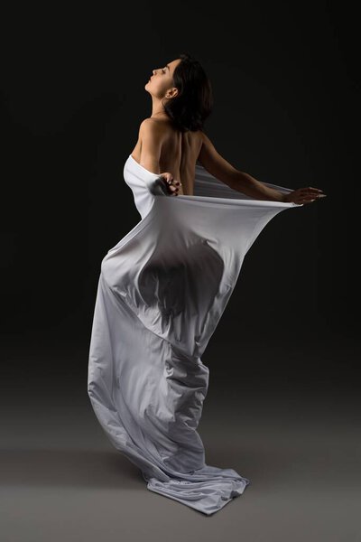 Seductive woman in white cloth standing gracefully in studio