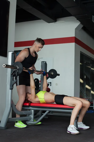 Handsome man helps girl with barbell exercise — Stock Photo, Image