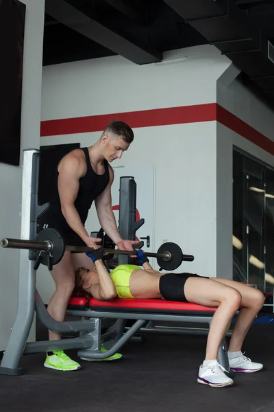 Antrenorul asigură o femeie tânără care exercită cu barbell — Fotografie, imagine de stoc