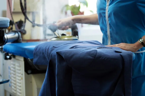 Laundry worker steaming jacket on ironing board — Stock Photo, Image