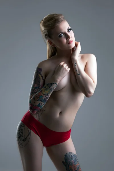 Busty dziewczyna tatuażem pozuje w czerwone majtki — Zdjęcie stockowe