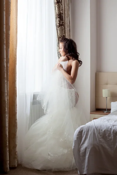 La sposa mezza vestita guarda pensierosamente la finestra — Foto Stock