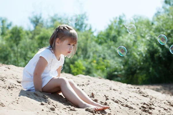 Nieuwsgierig weinig model zittend op zand in park — Stockfoto