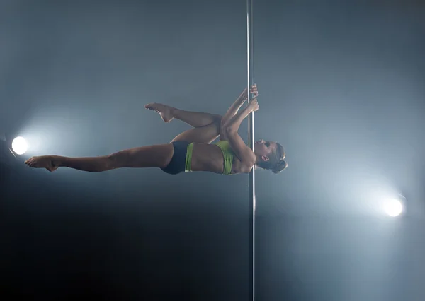 Strong girl dancing on pole in rays of spotlights — Stock Photo, Image