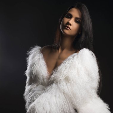 Sadece bir sandalye görünümü gri arka plan üzerinde oturan beyaz kürk palto giyiyor güzel esmer