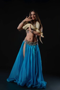 Bir kadın, elinde bir yılanla stüdyoda dans ediyor. Mavi bir etek giyiyor ve kendine güvenerek poz veriyor. Ayar onun hareketlerine ve yılanına güçlü bir odaklanma sağlıyor..