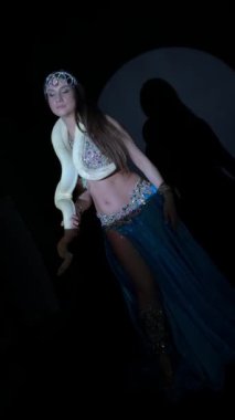 Bu büyüleyici videoda büyüleyici bir göbek dansı kostümü giymiş bir kadın büyük bir albino pitonu ile zarif bir şekilde poz veriyor ve hareket ediyor. Dramatik spot ışıkları gizemli, egzotik bir atmosfer yaratır..