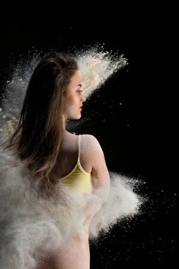 Siyah arka planda dans ederken kum bulutunda duran iç çamaşırlı çekici genç bir kadın.