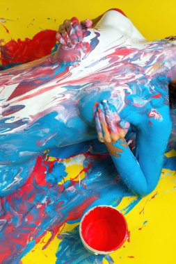 Bir insan parlak boyayla kaplıdır, sarı bir yüzeyde sanatsal bir görüntü yaratır, yaratıcılığı ve kendini ifade etmeyi ön plana çıkarır..