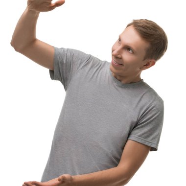 Genç bir adam beyaz bir arka plana karşı duruyor, gülümsüyor ve sanki elinde görünmez bir nesneyi tutuyor ya da sunuyor gibi hareket ediyor..