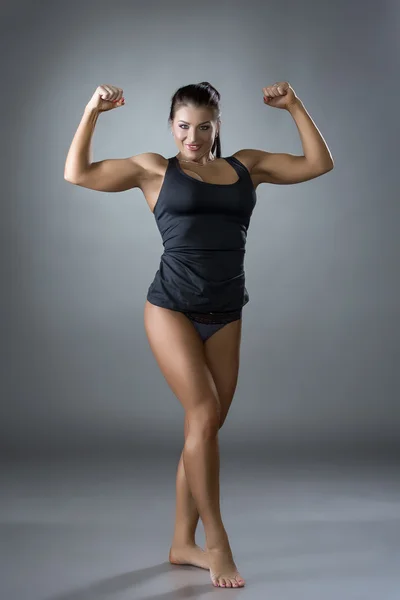 Muskulöse Frau posiert im Studio vor grauem Hintergrund — Stockfoto