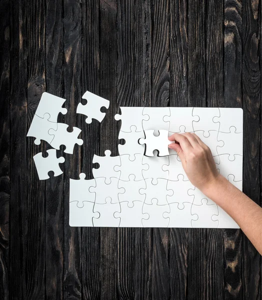 Hand collecting white puzzle on black background — Stock Photo, Image