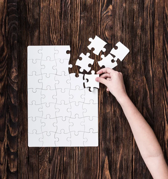 Hand collecting white puzzle on brown background — Stock Photo, Image