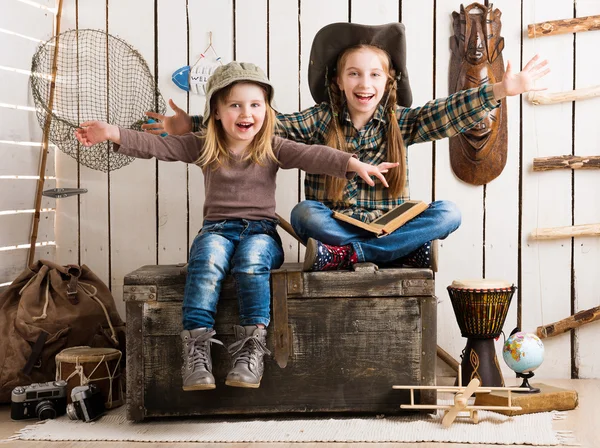Dos niñas sentadas en el pecho de madera con las manos arriba — Foto de Stock