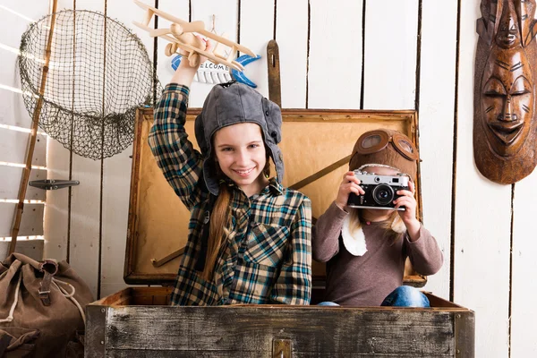 Linda niña tomando fotos de otra niña pequeña en el pecho de madera — Foto de Stock